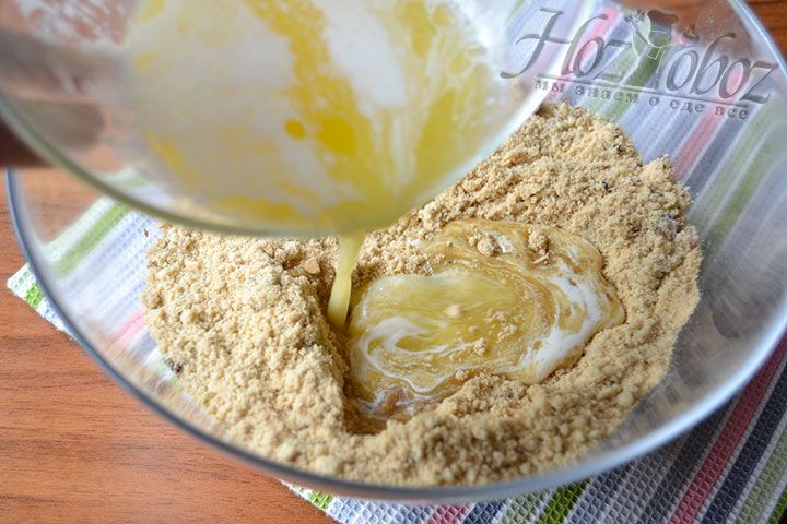 Поместите сливочное масло в жидком состоянии в миску с песочной крошкой и дроблеными орехами