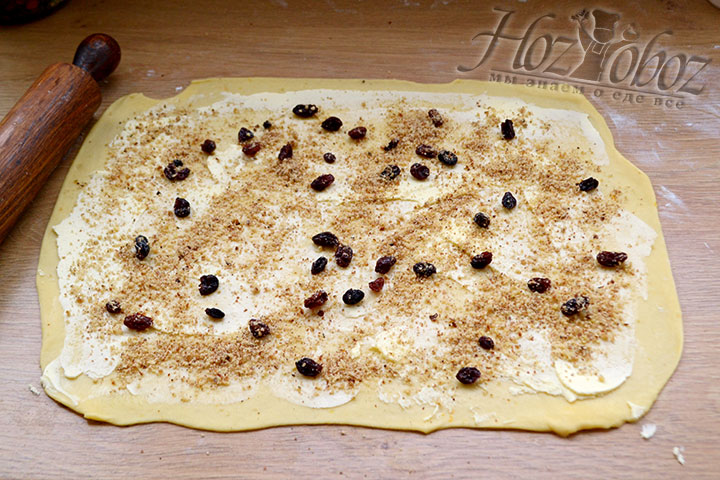 Раскатываем скалкой тесто в прямоугольник, наносим на всю поверхность широкой лопаткой сливочное масло, распределяем изюм и орехи.